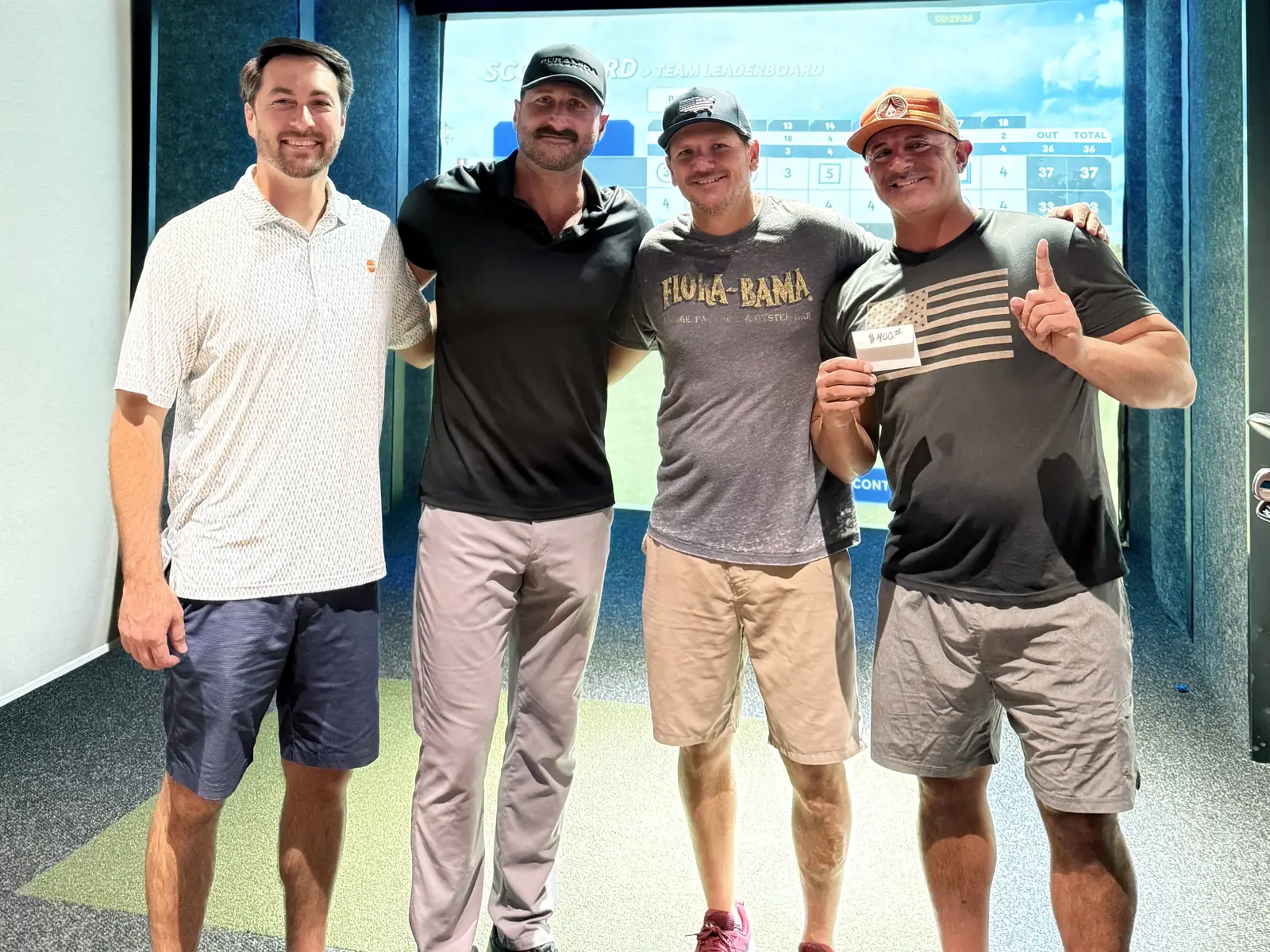 Four golfers in a Swing Suite bay at Tee Off at The Wharf, facing the camera