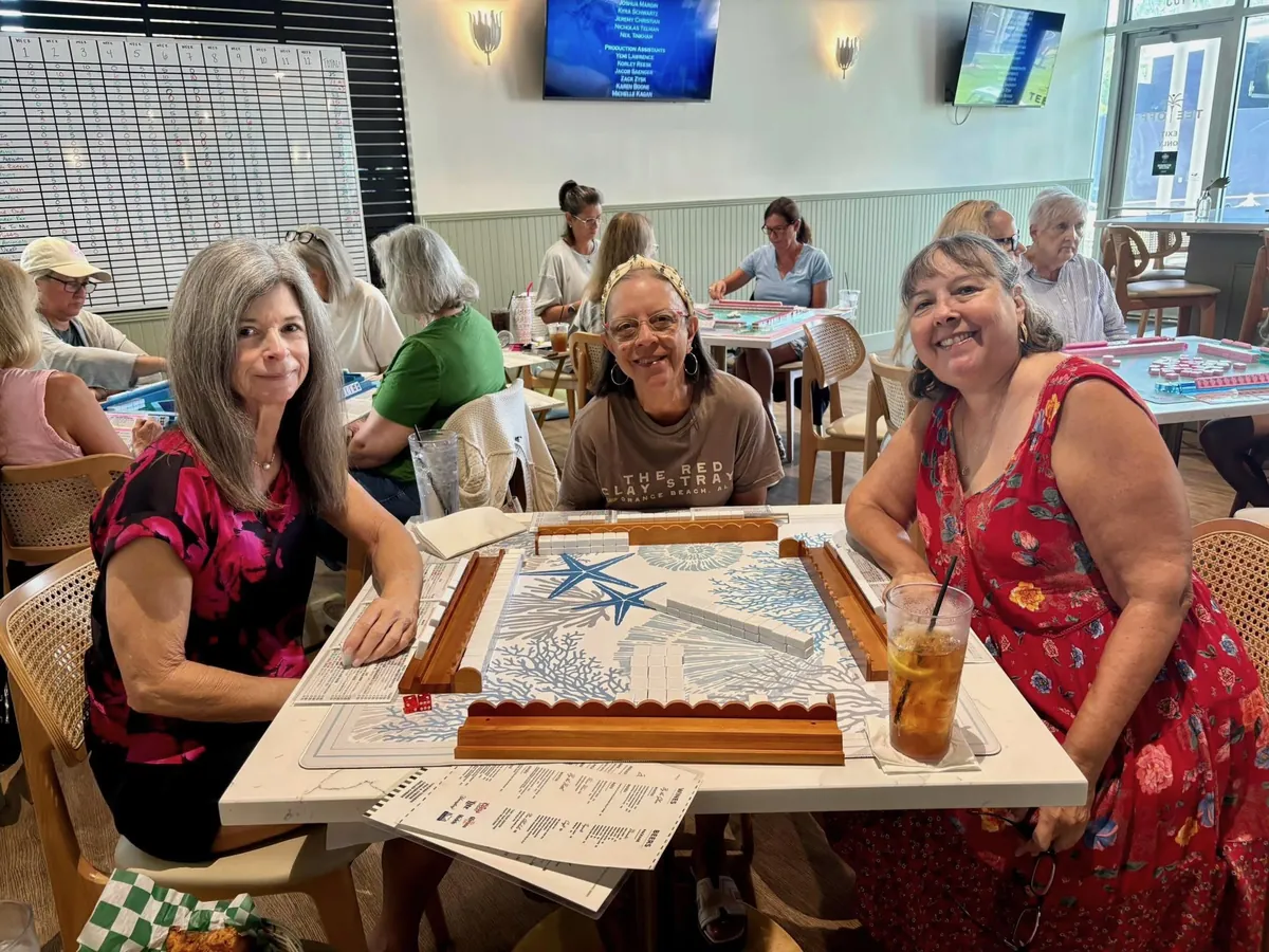 Three players smiling over a mahjong table at Tee Off at The Wharf, tiles set up on racks