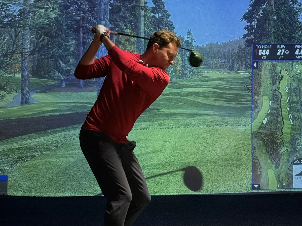 A golfer mid-backswing against a pine-lined hole on the screen at Tee Off at The Wharf