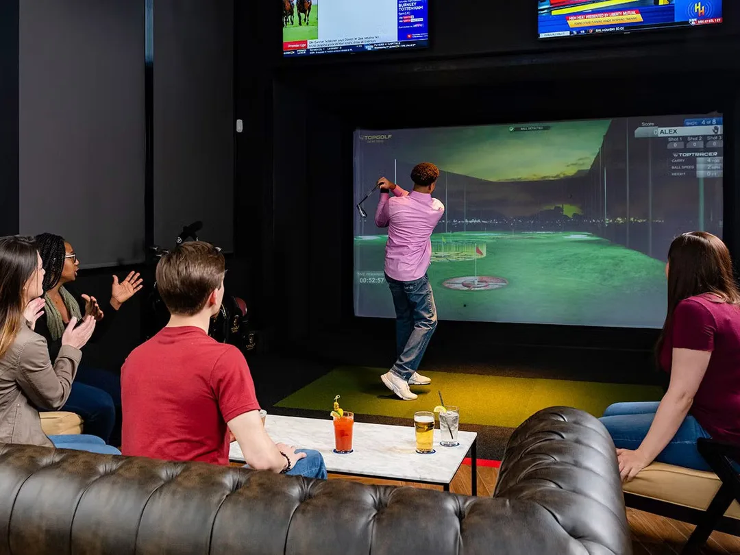 A group watching a golfer take a swing in a Swing Suite bay at Tee Off at The Wharf