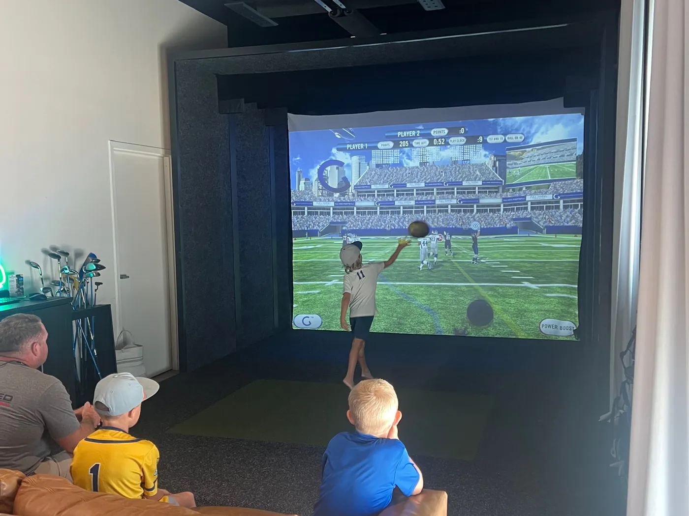 A player throwing a pass in a bay at Tee Off at The Wharf, receivers and a play clock on the screen